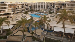 Un complejo turístico con varias edificaciones, una piscina central, palmeras y zonas de estar al aire libre.
