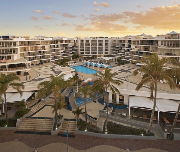 Ein Resort mit mehreren Gebäuden, einem zentralen Pool, Palmen und Sitzbereichen im Freien.