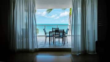 A room with a view of the ocean through sheer curtains, a small table with chairs, and a tiled floor.
