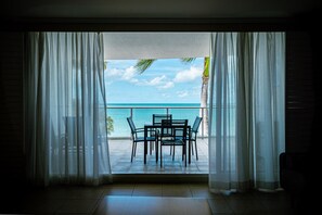 Une pièce avec vue sur l’océan, visible à travers de fines rideaux, une petite table avec des chaises et un sol carrelé.