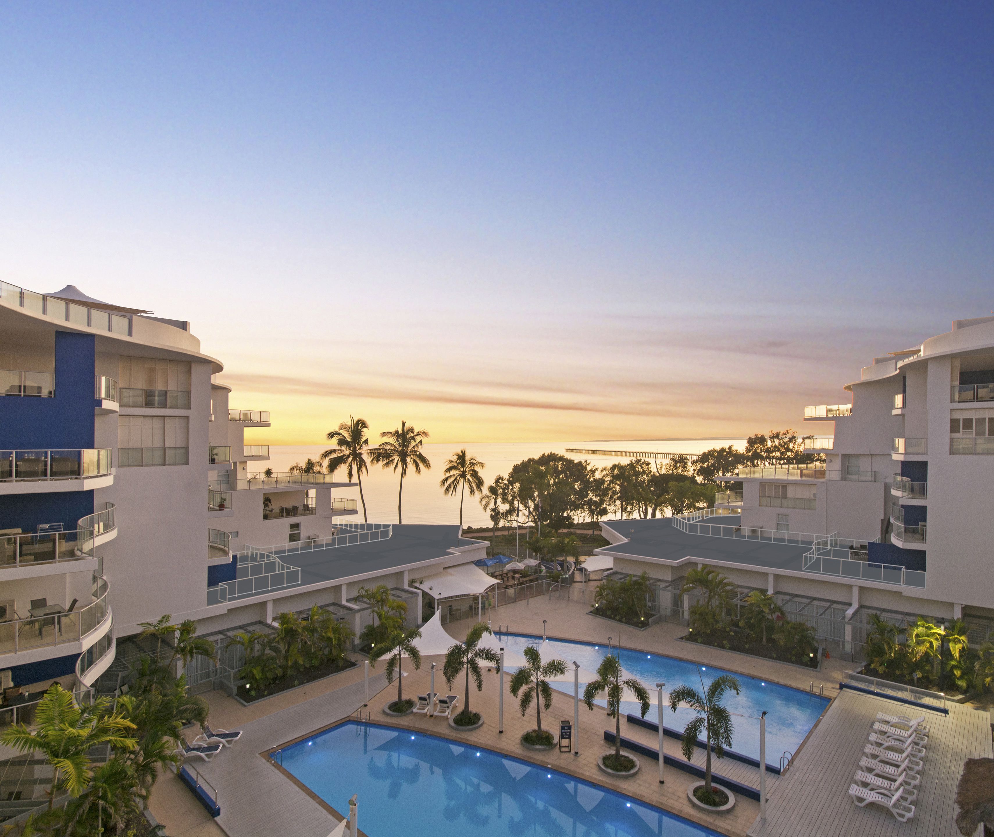 Un resort con piscina, palmeras y vistas al atardecer.