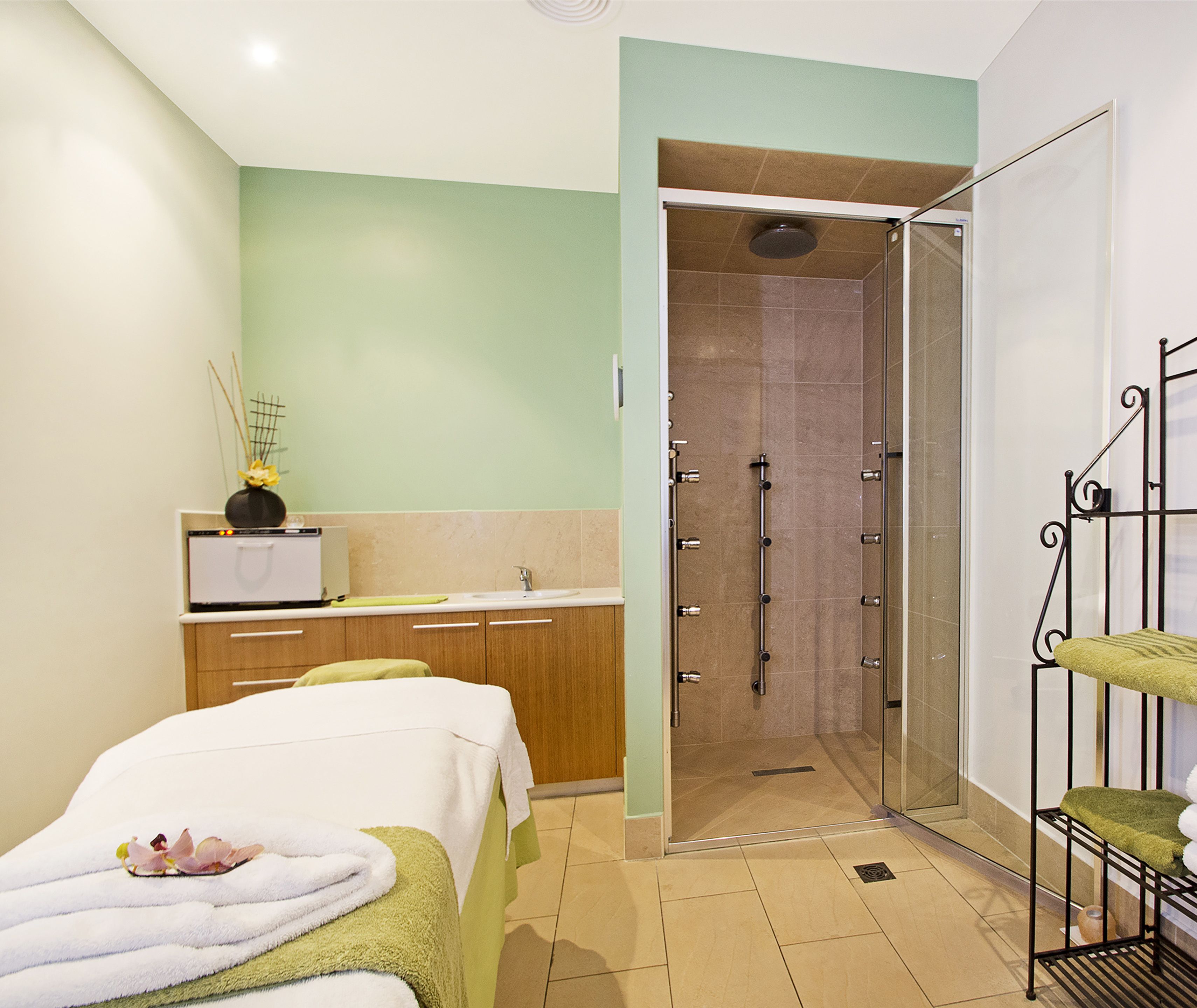 A modern bathroom with a shower, a sink, and a bed with towels.