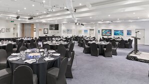 Een ruime conferentieruimte met meerdere ronde tafels, elk voorzien van stoelen, borden, glazen en bestek.