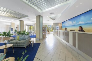 A hotel lobby with a reception desk, seating area, and a large window with a view of the outdoors. - Oaks Hervey Bay Resort and Spa (Urangan)