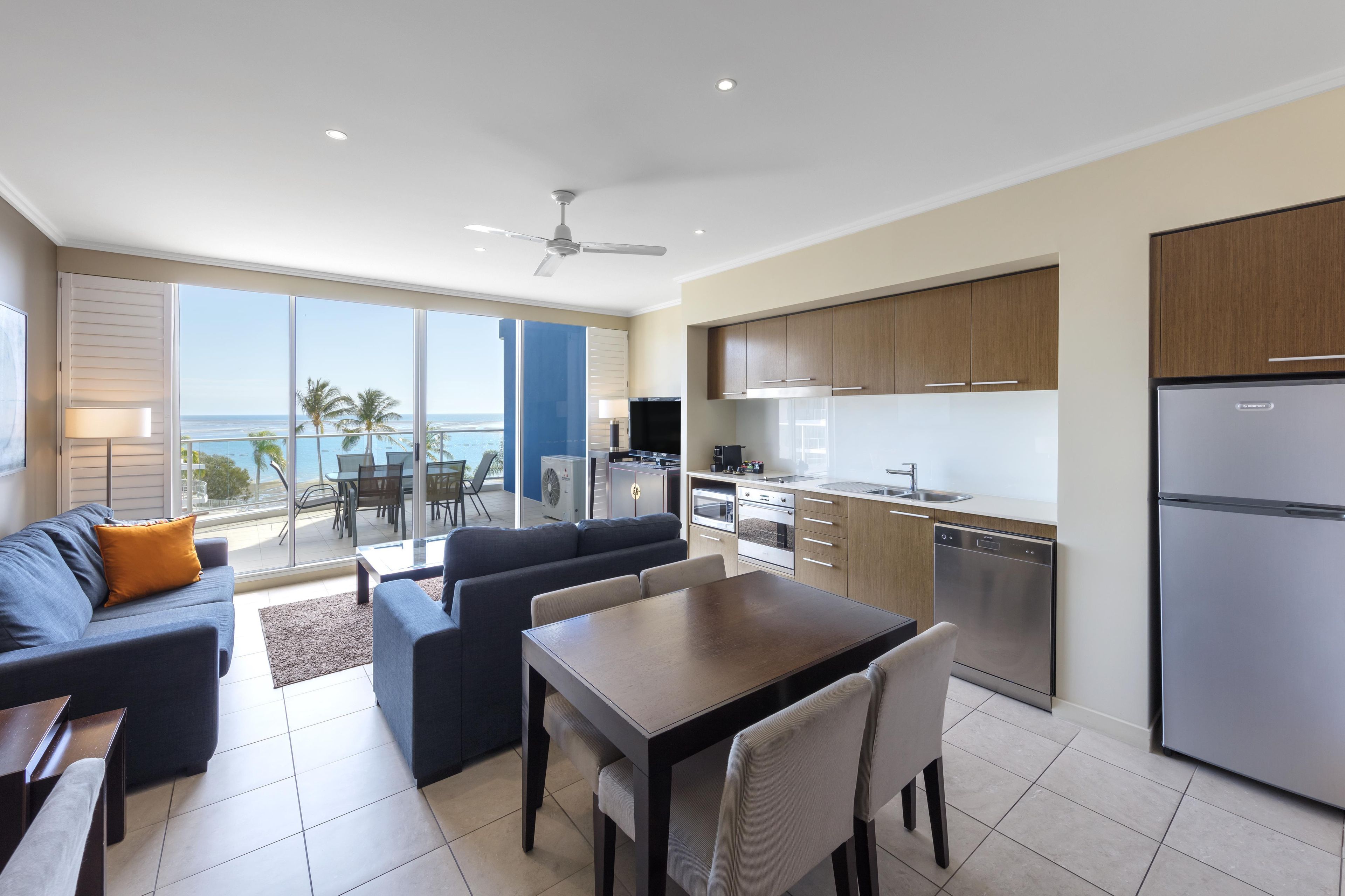 A modern kitchen with a built-in dishwasher, a dining area with a table and chairs, and a balcony with a view of the ocean.