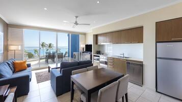 A modern kitchen with a built-in dishwasher, a dining area with a table and chairs, and a balcony with a view of the ocean.