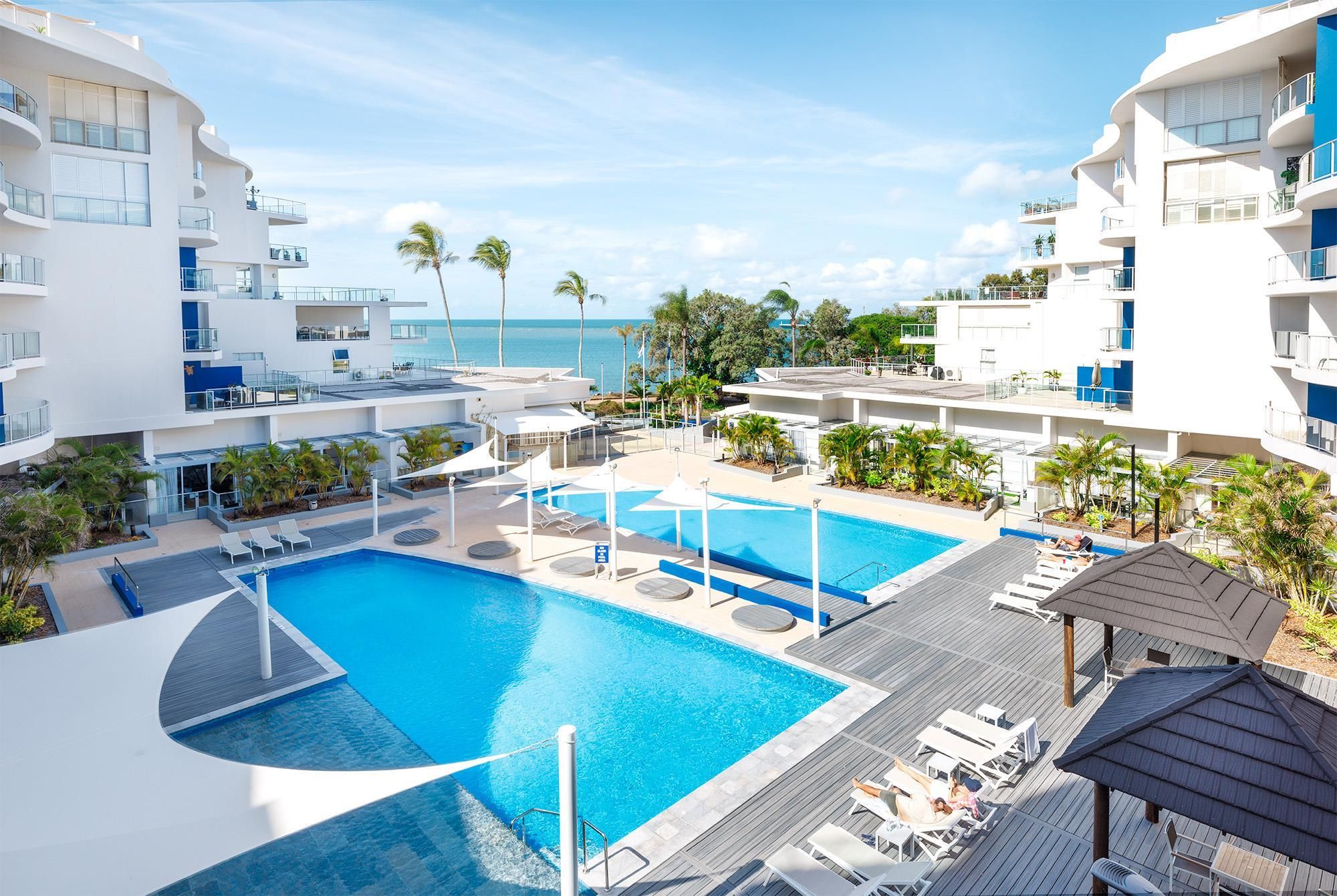 Un resort con una gran piscina, tumbonas y vista al océano.