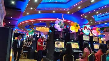Interior de un casino con máquinas tragamonedas, luces de techo coloridas y globos decorativos.