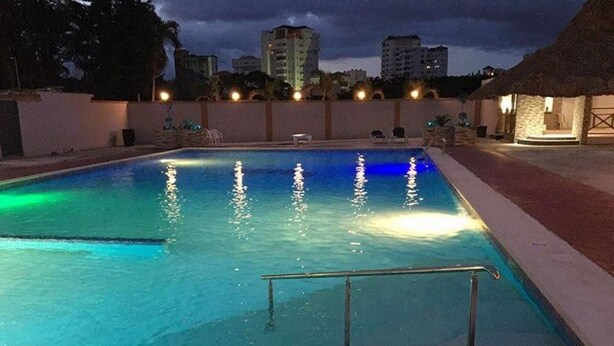 Una piscina con barandilla de metal, rodeada por un muro bajo y una estructura de techo de paja.