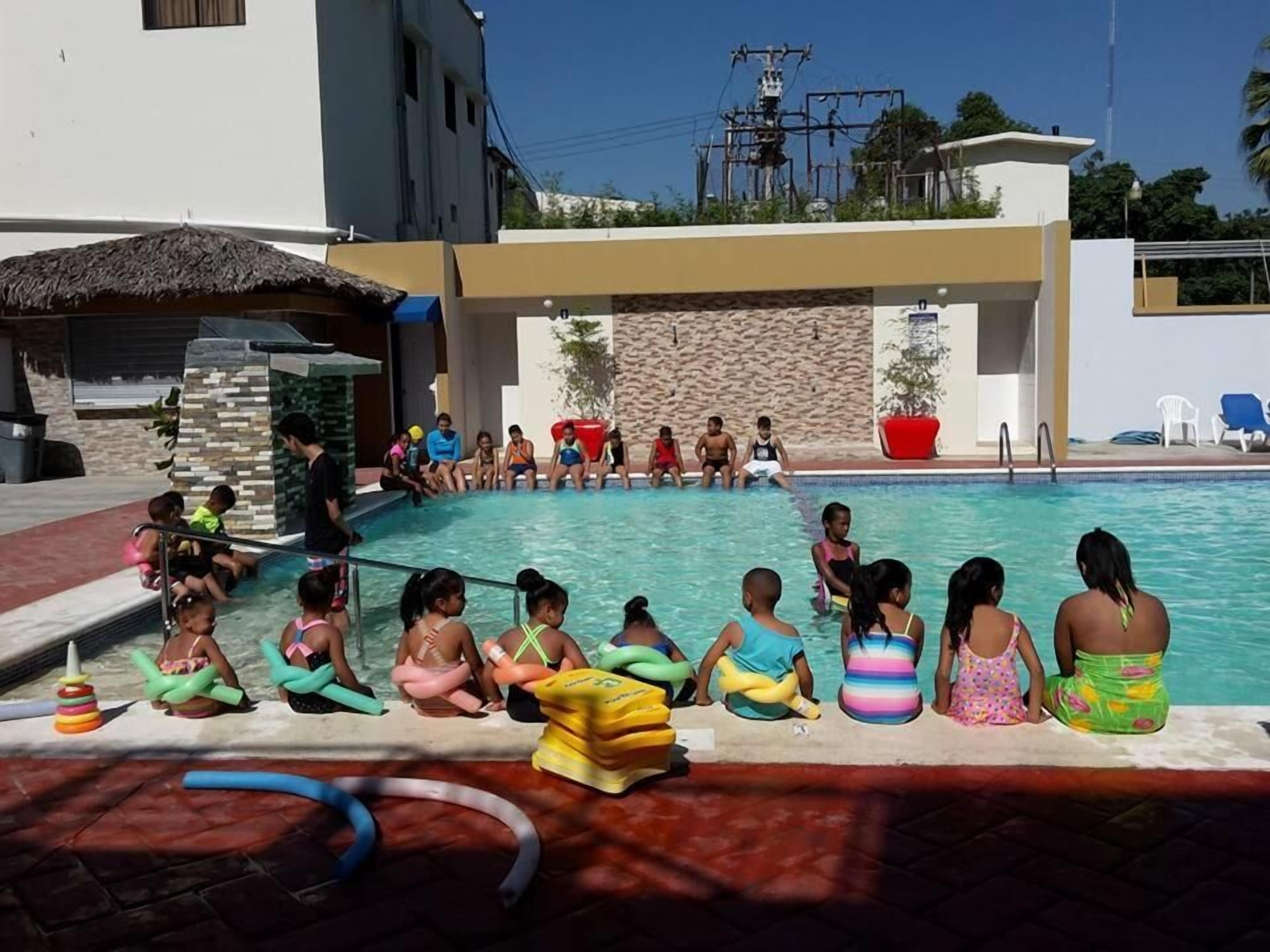 Ein Schwimmbecken mit Kindern und Erwachsenen, die am Rand sitzen.
