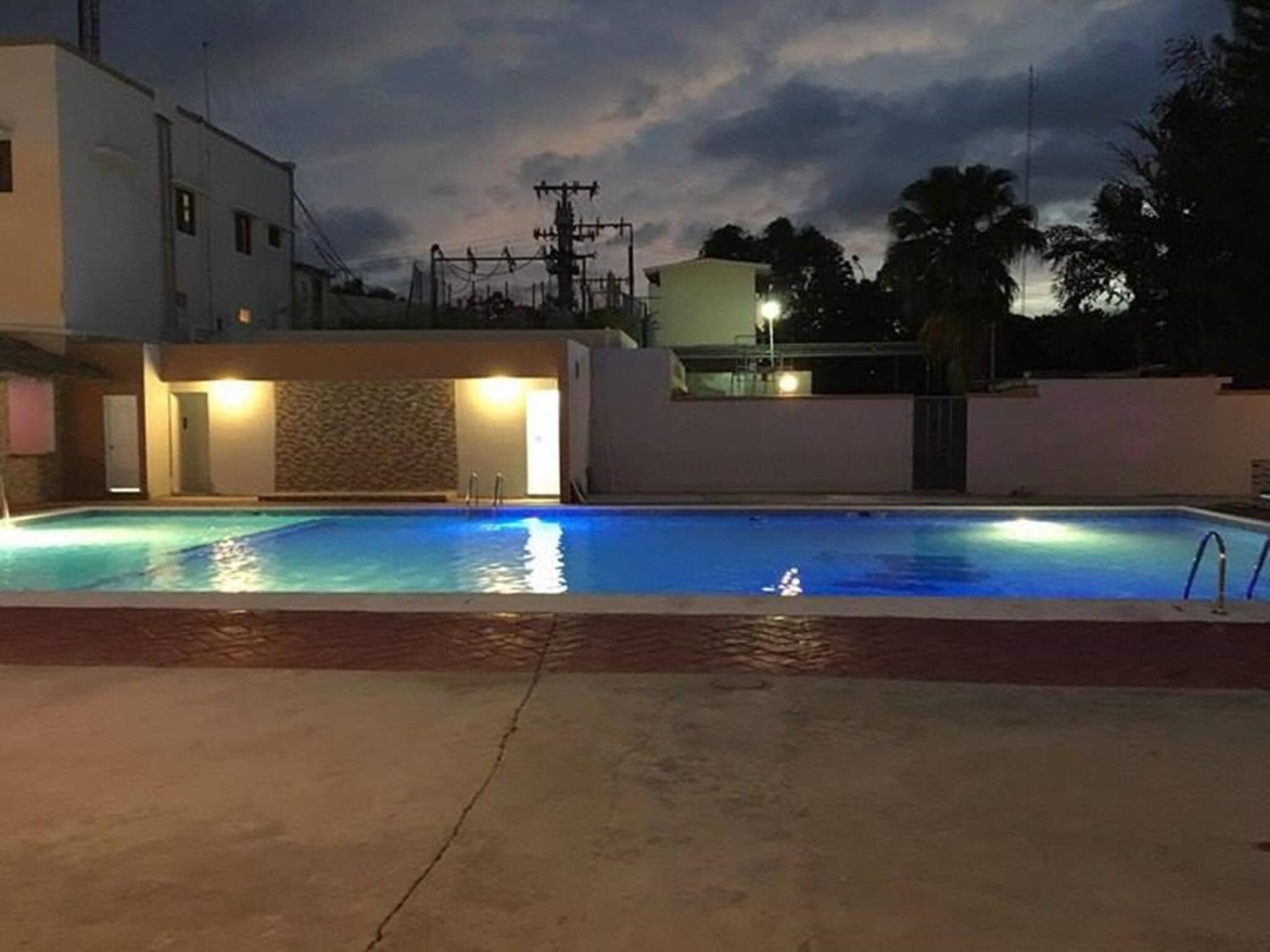 A swimming pool with a stone wall and a building with a balcony in the background.