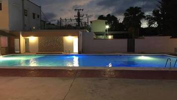 Une piscine avec un mur en pierre et, au fond, un bâtiment doté d’un balcon.