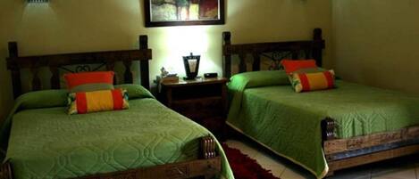 Two single beds with wooden frames and green bedding, a nightstand with a lamp, and a painting on the wall.