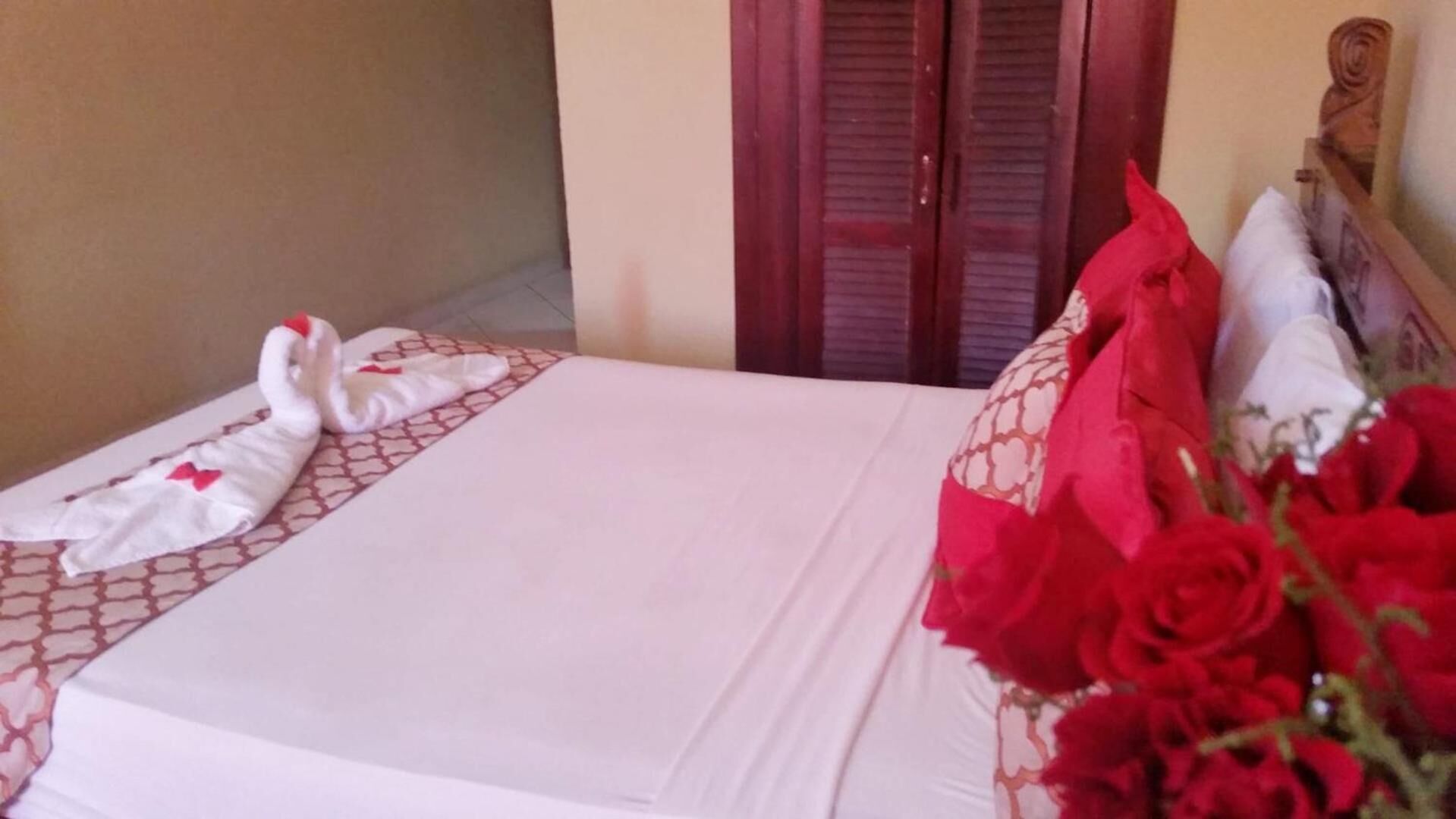 Una habitación de hotel con una cama, una puerta de madera y un ramo de rosas rojas sobre la cama.