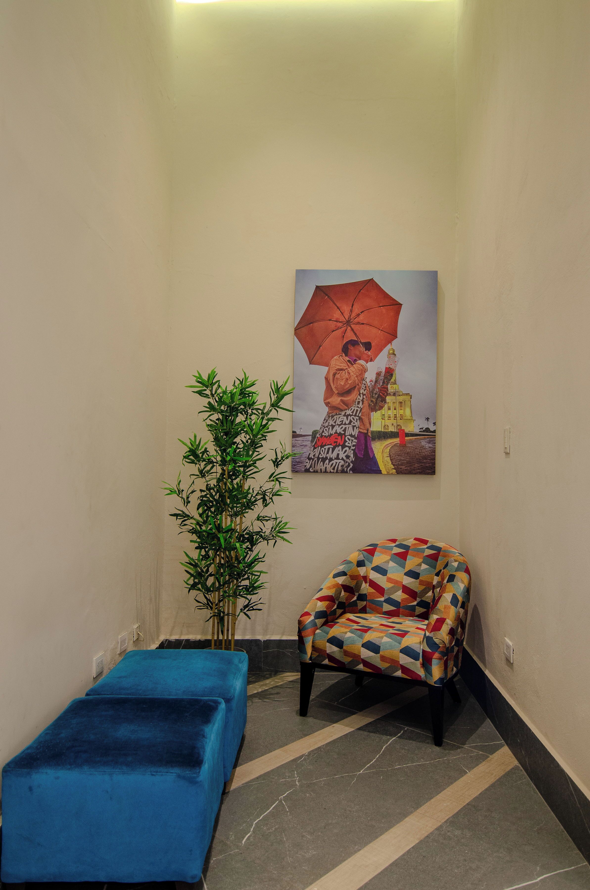 A room with a blue bench, a colorful armchair, a bamboo plant, and a painting of a person with an umbrella.