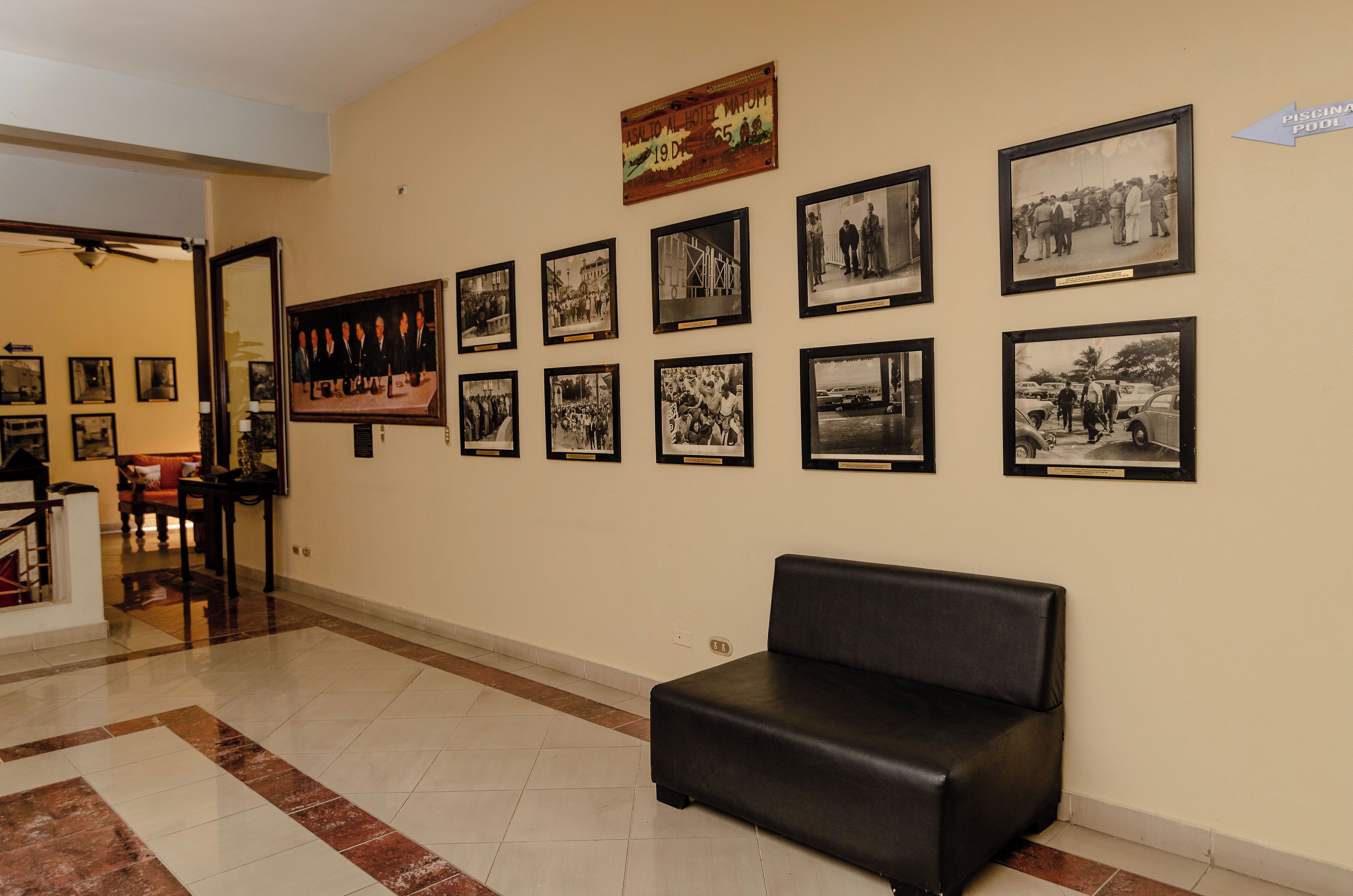 Un vestíbulo con un sofá de cuero negro, piso de baldosas y una pared decorada con fotografías blanco y negro enmarcadas.