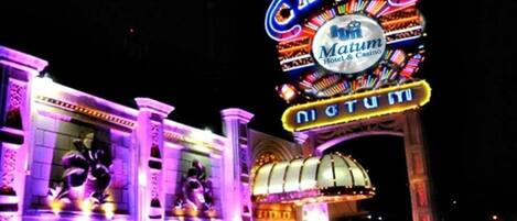 Una entrada de casino muy iluminada con un letrero de neón que dice 'Casino Matum Hotel & Casino' y 'Digi Tumi'.