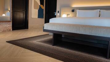 Quarto de hotel moderno com uma cama grande, uma cabeceira de madeira escura, um tapete texturizado e uma luminária fixada na parede.