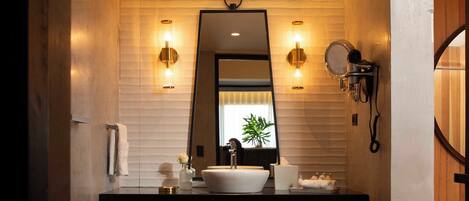 Un baño moderno con encimera negra, lavamanos blanco y dos luces empotradas.