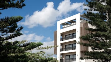 A modern multi-story building with balconies, surrounded by trees and under a clear sky.