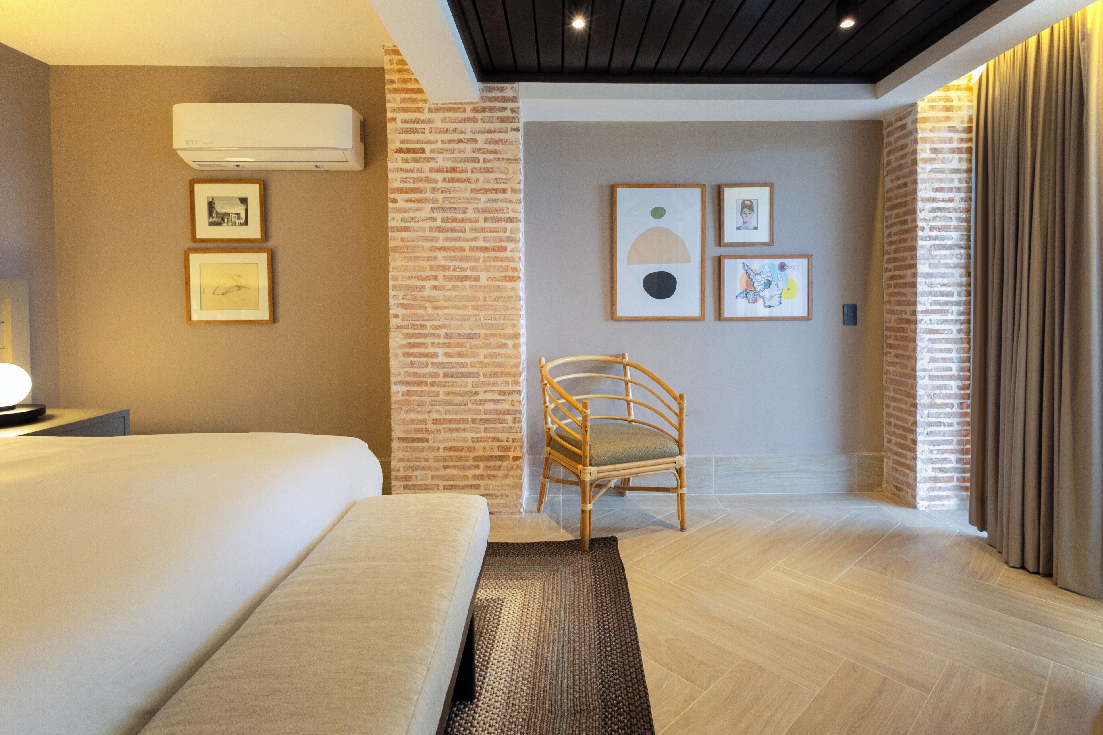Habitación de hotel con cama, una silla, aire acondicionado de pared y obras de arte enmarcadas.