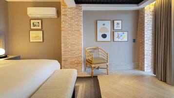 Habitación de hotel con cama, una silla, aire acondicionado de pared y obras de arte enmarcadas.