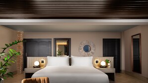 A modern hotel room with a large bed, bedside tables with lamps, a mirror, and a potted plant. - Camp David Ranch (Santiago de los Caballeros)