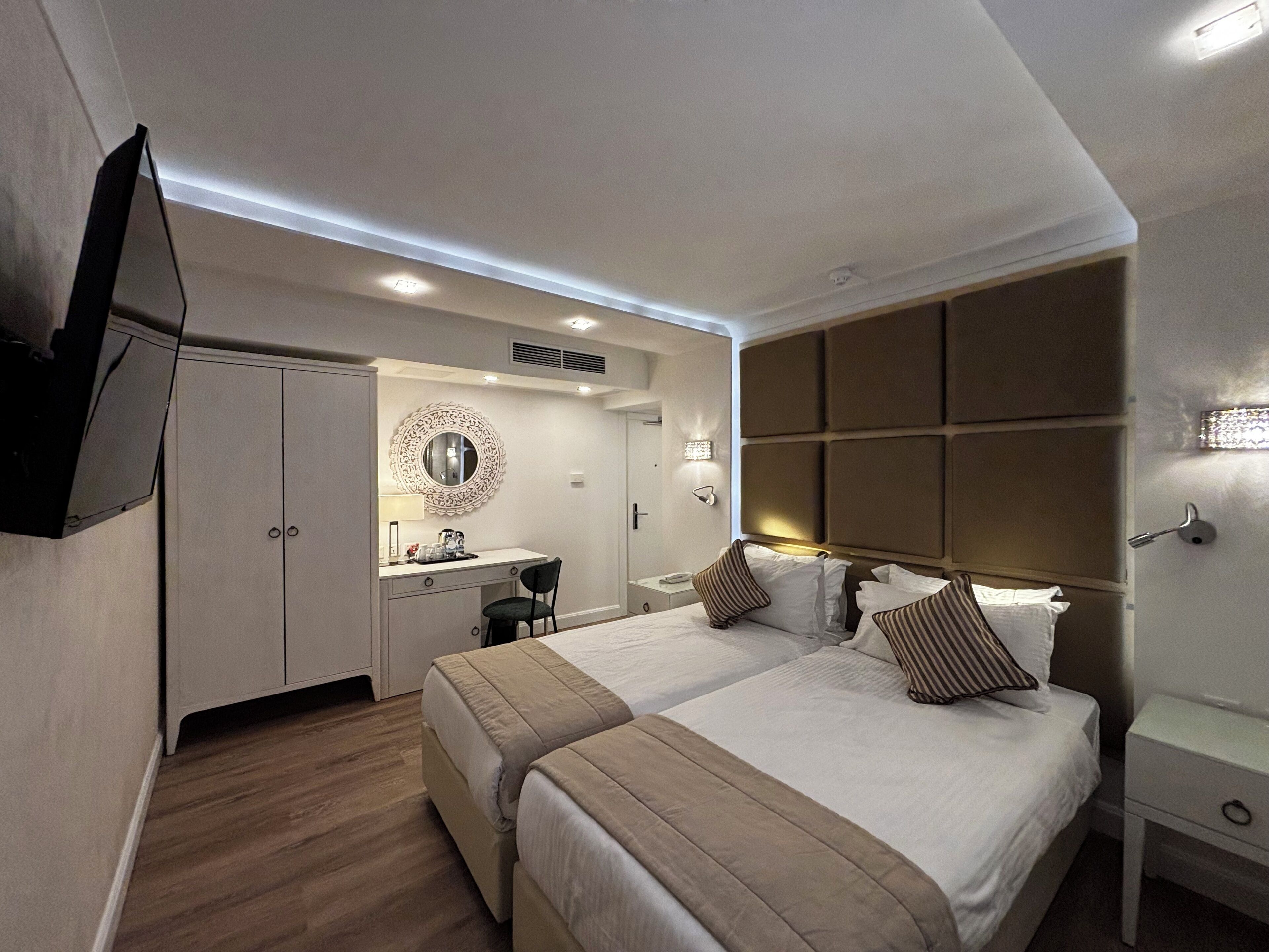 Habitación de hotel con una cama grande, un escritorio con silla, tocador con espejo y televisor montado en la pared.