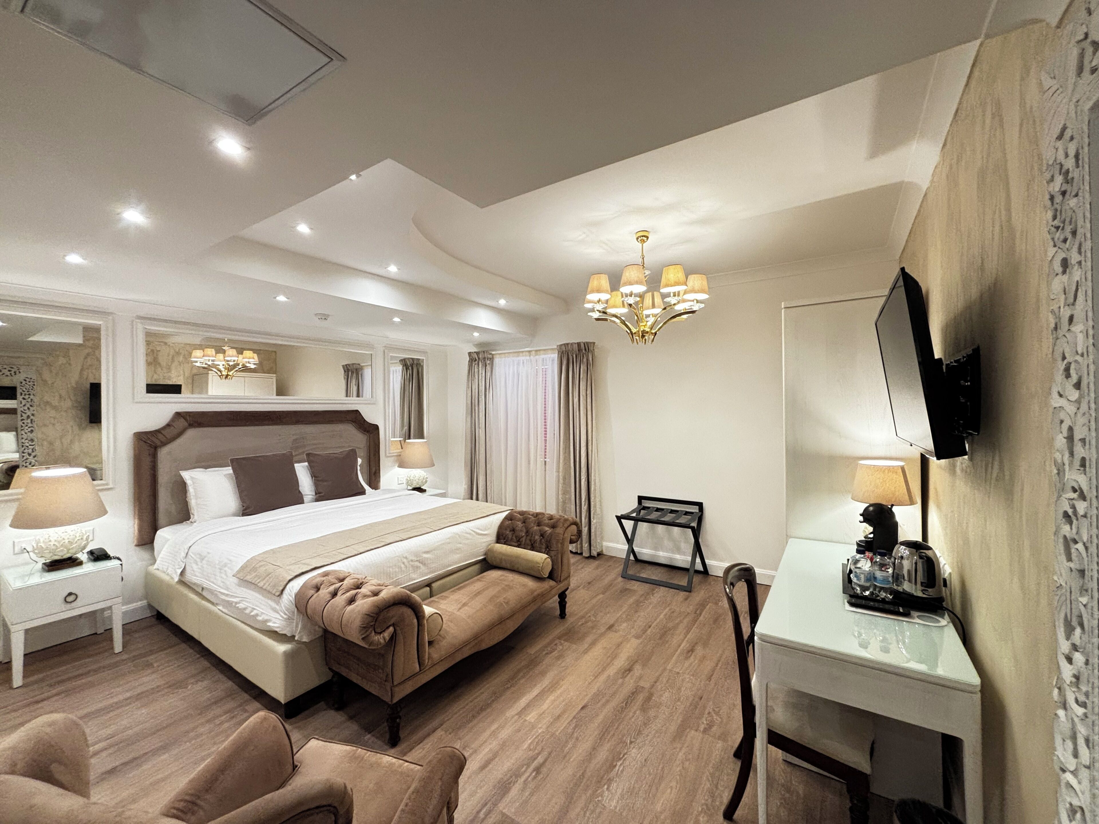 Een hotelkamer met een groot bed, nachtkastjes, een bureau, een stoel, een televisie en een kroonluchter.