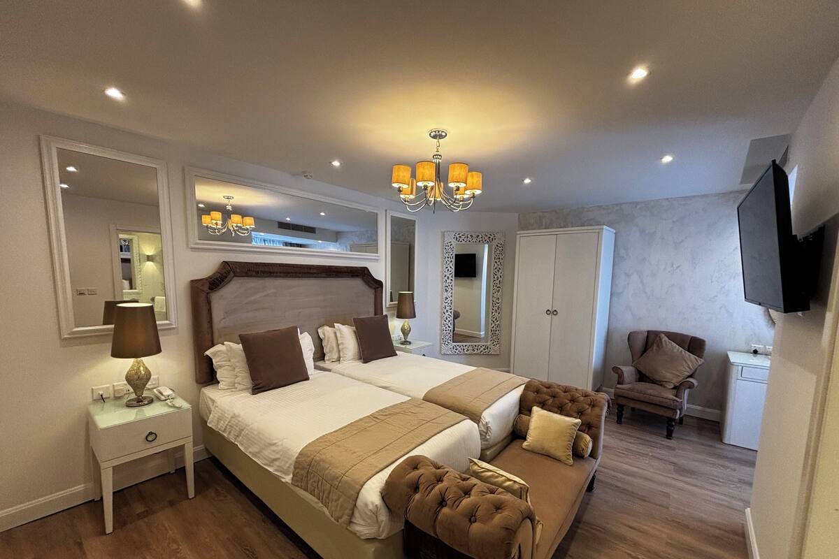 A double bed with a headboard, bedside tables, a mirror, a TV, a wardrobe, a chair, and a chandelier.