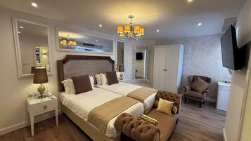 A double bed with a headboard, bedside tables, a mirror, a TV, a wardrobe, a chair, and a chandelier.