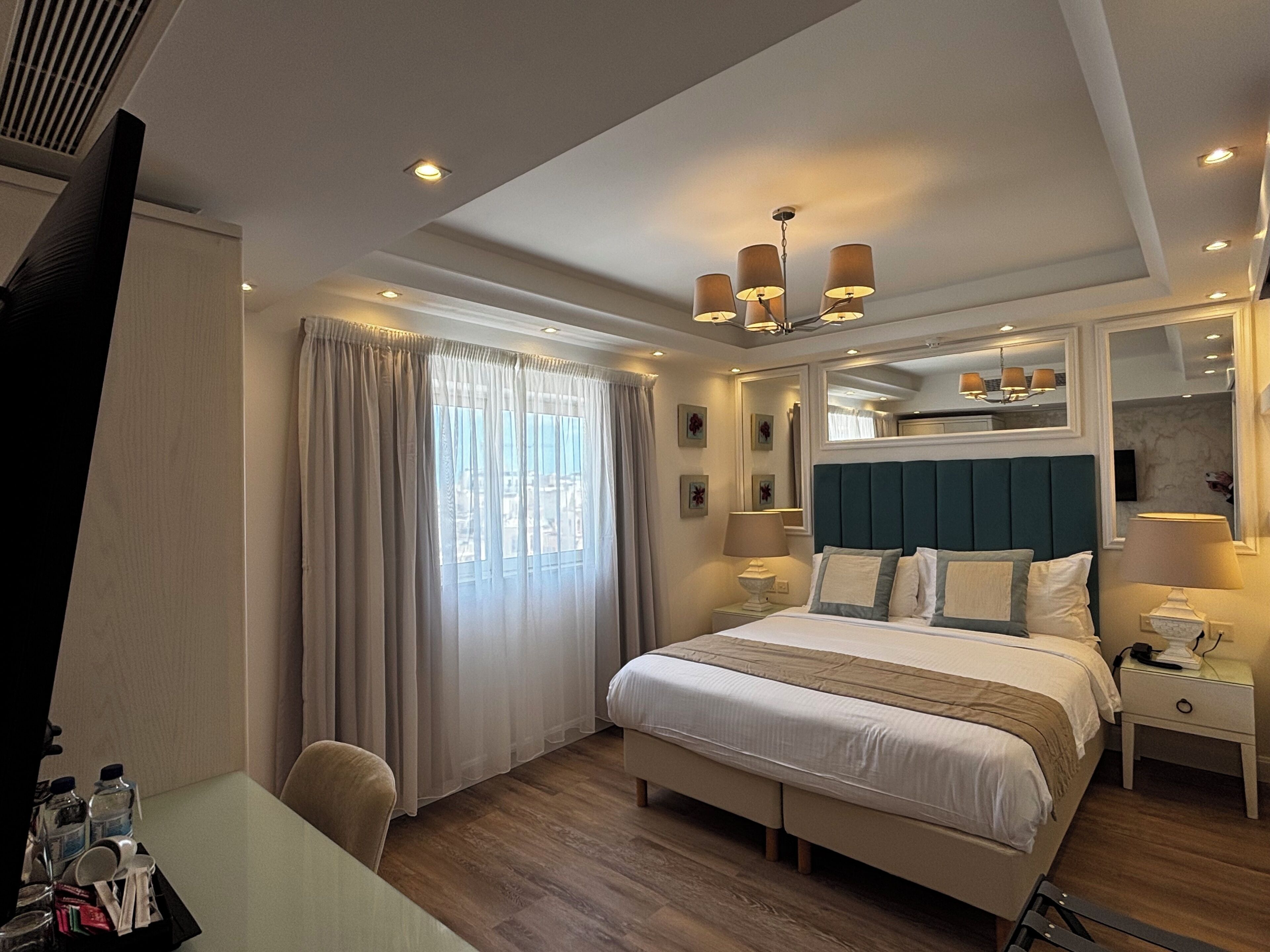 Una habitación de hotel con cama, mesitas de noche, escritorio y ventana con cortinas.