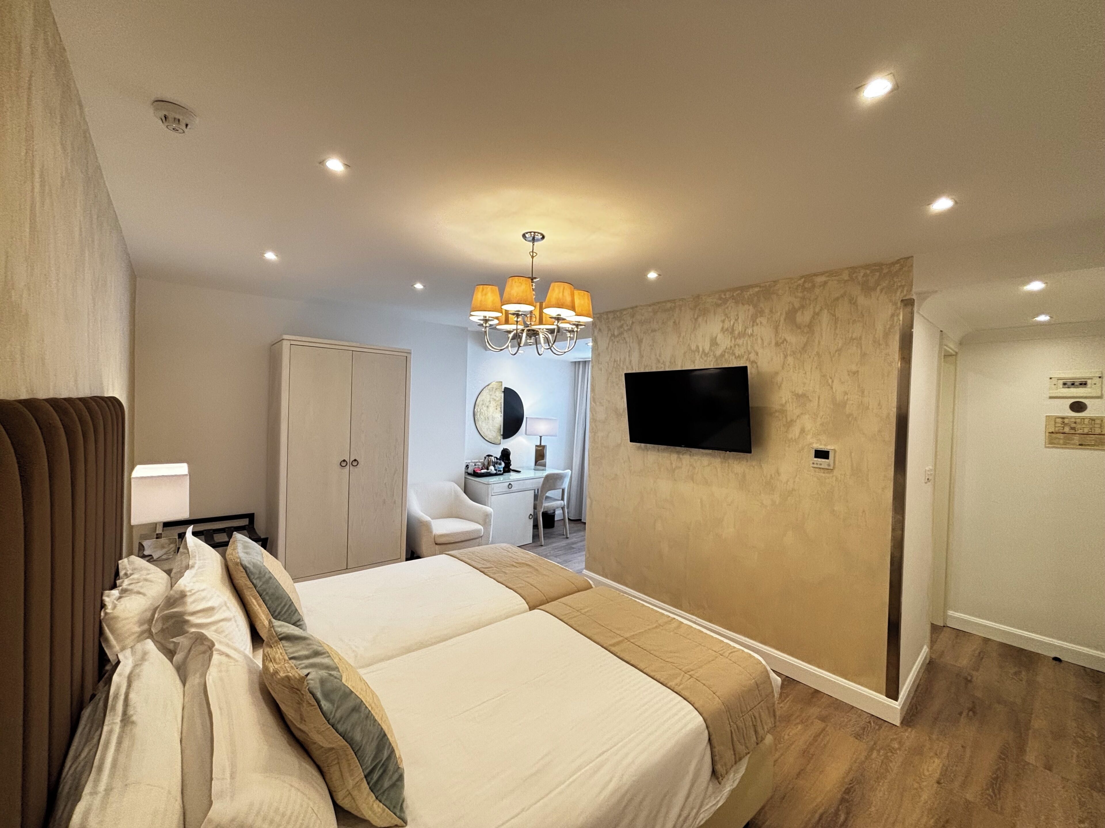 Habitación de hotel con una cama grande, un armario, un escritorio con una silla, un televisor y un baño al fondo.