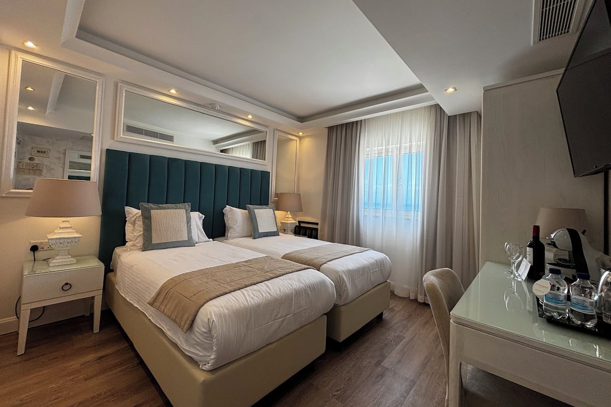 A hotel room with two beds, a desk, a chair, a TV, and a window with curtains.