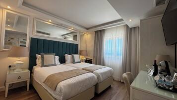Habitación de hotel con dos camas, un escritorio, una silla, un televisor y una ventana con cortinas.