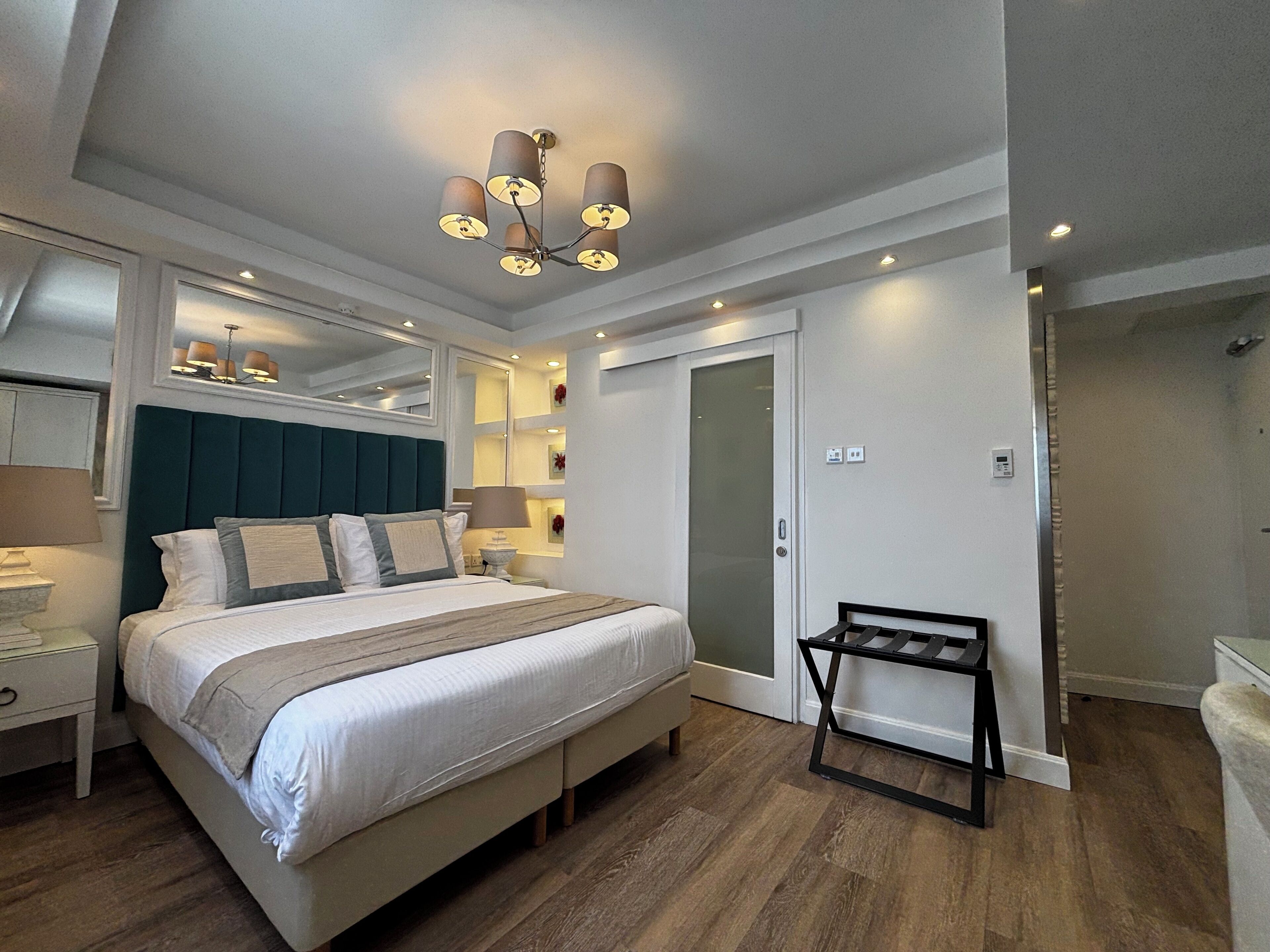 A bedroom with a bed, bedside tables, a mirror, a dresser, a bench, and a door with a frosted glass panel.
