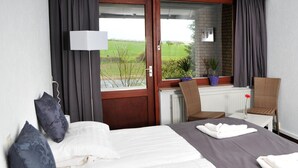 Ein Hotelzimmer mit Bett, Stuhl, Vorhängen am Fenster und Blick ins Freie.