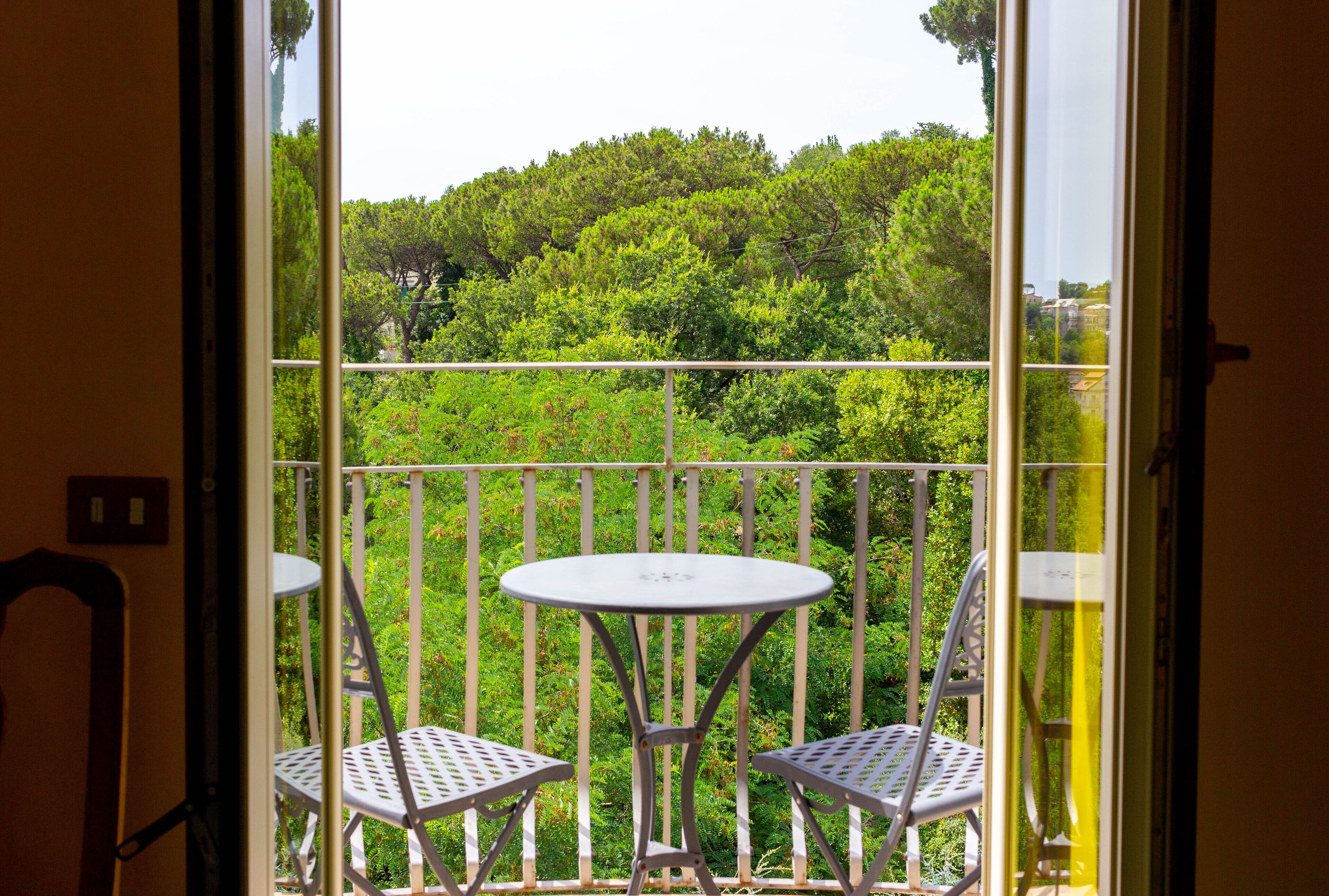 Een balkon met een witte metalen tafel en twee stoelen, met uitzicht op een weelderig groen landschap.