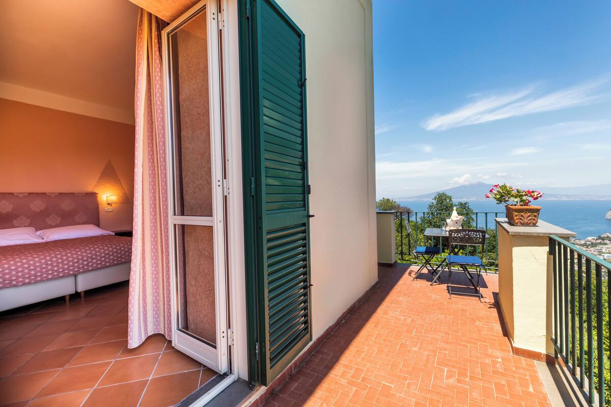 Ein Balkon mit einem Bett, einem Tisch mit Stühlen und Blick aufs Meer.