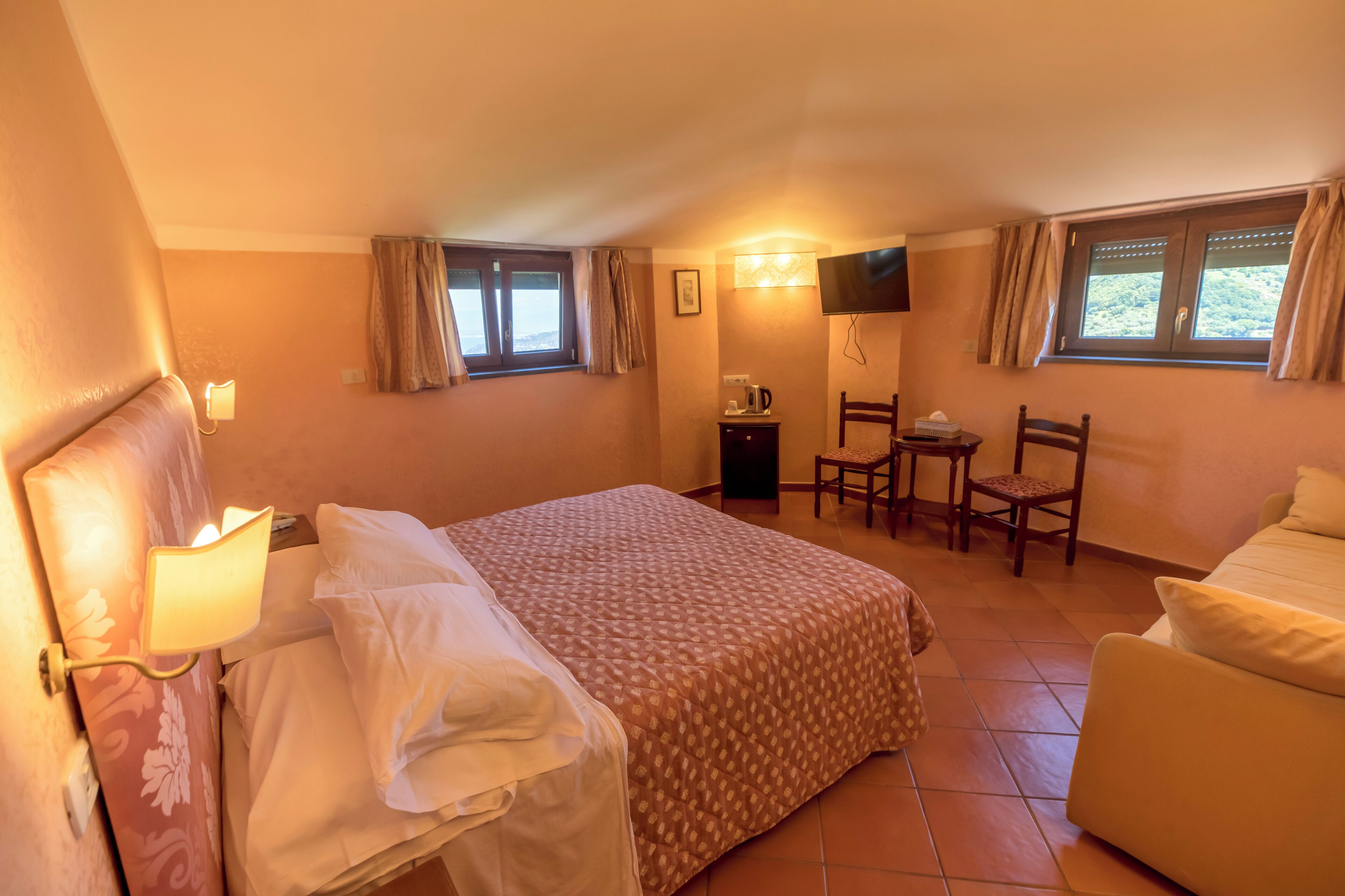 A hotel room with a bed, a desk, a chair, a TV, and a window with curtains.