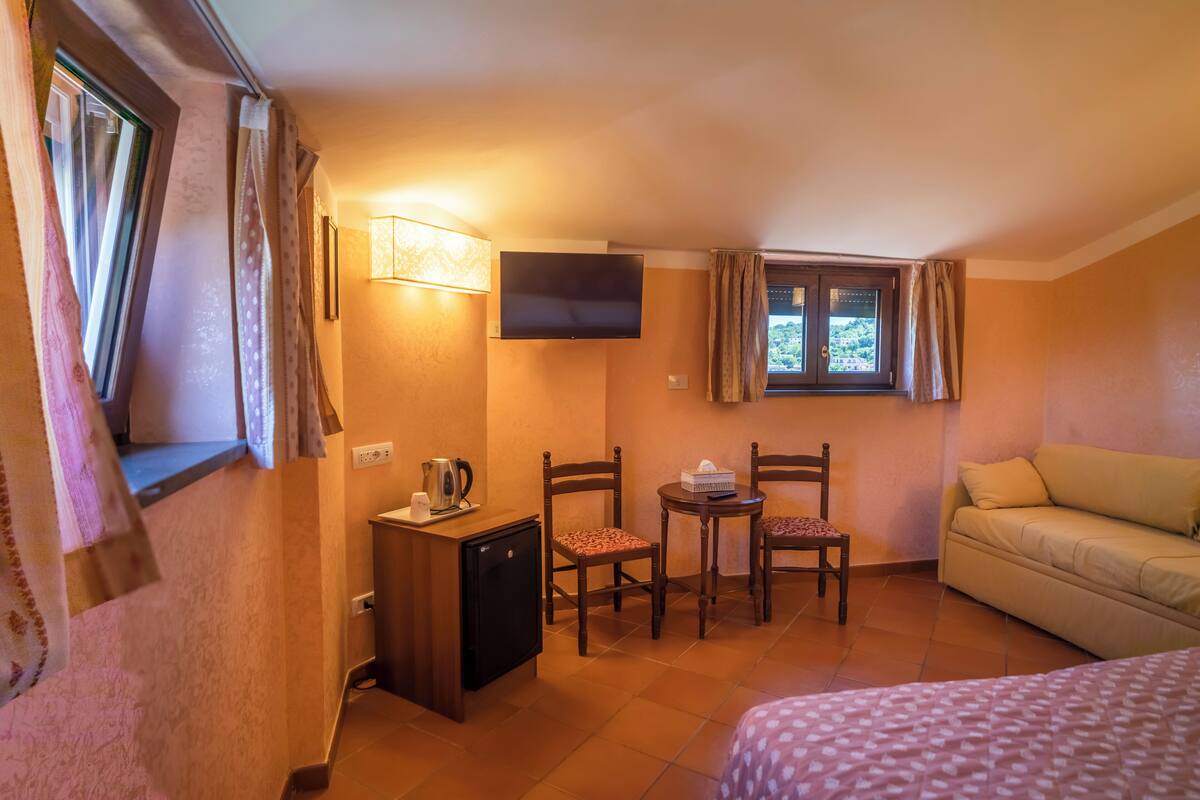 Ein Hotelzimmer mit Bett, einem kleinen Tisch mit Stühlen, einem Fernseher, einem Fenster mit Vorhängen und einem Sofa.