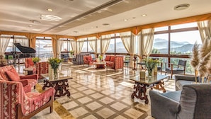A spacious lounge with a piano, comfortable seating, and large windows offering mountain views. - Grand Hotel Hermitage & Villa Romita (Massa Lubrense)
