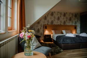A bedroom with a large bed, a bedside table, a nightstand, a window with curtains, and a vase with flowers on a table. - Waldhotel Kreuztanne (Sayda)