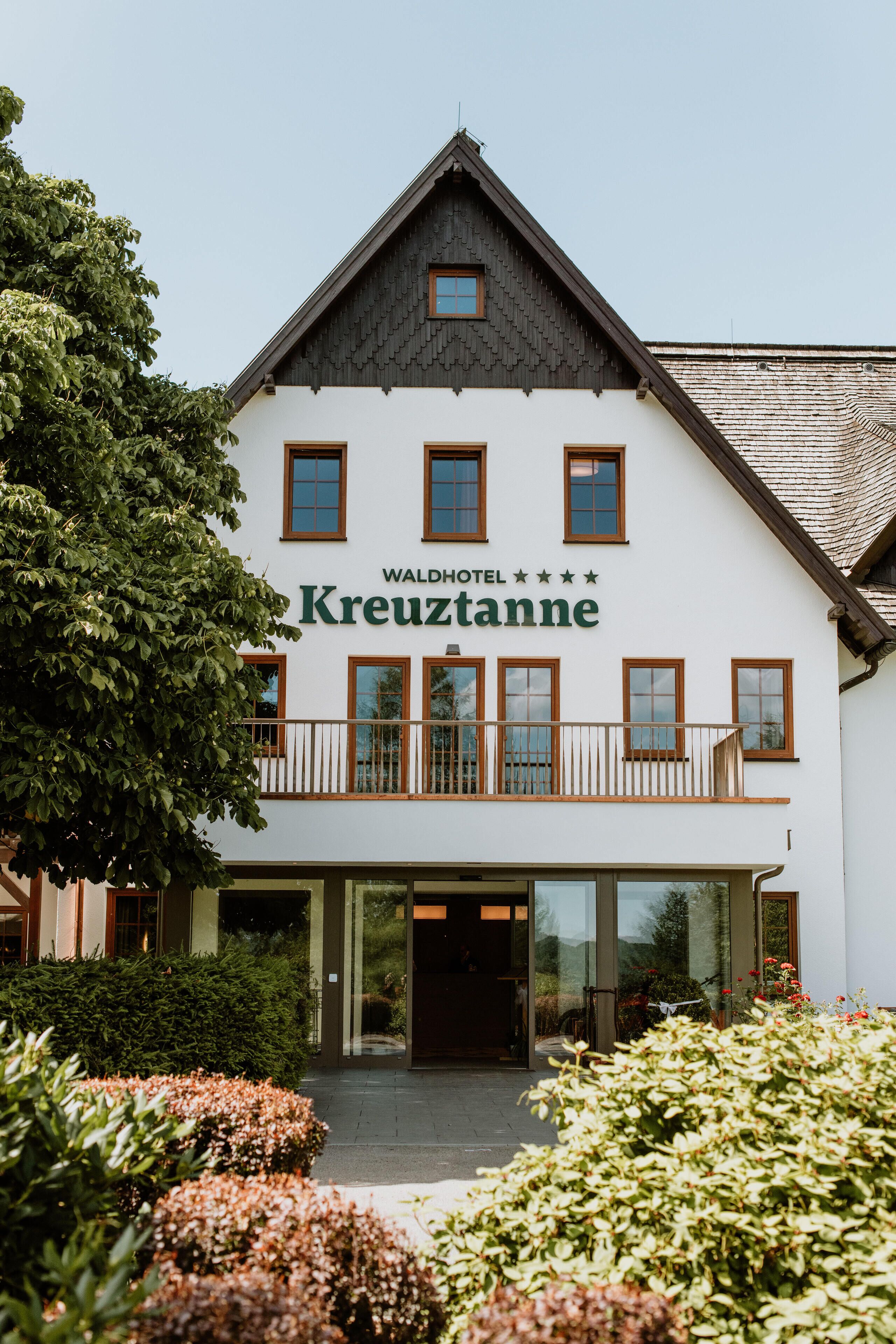 Un hôtel appelé « Waldhotel Kreuztanne », doté d’une façade blanche, de nombreuses fenêtres et d’un balcon.