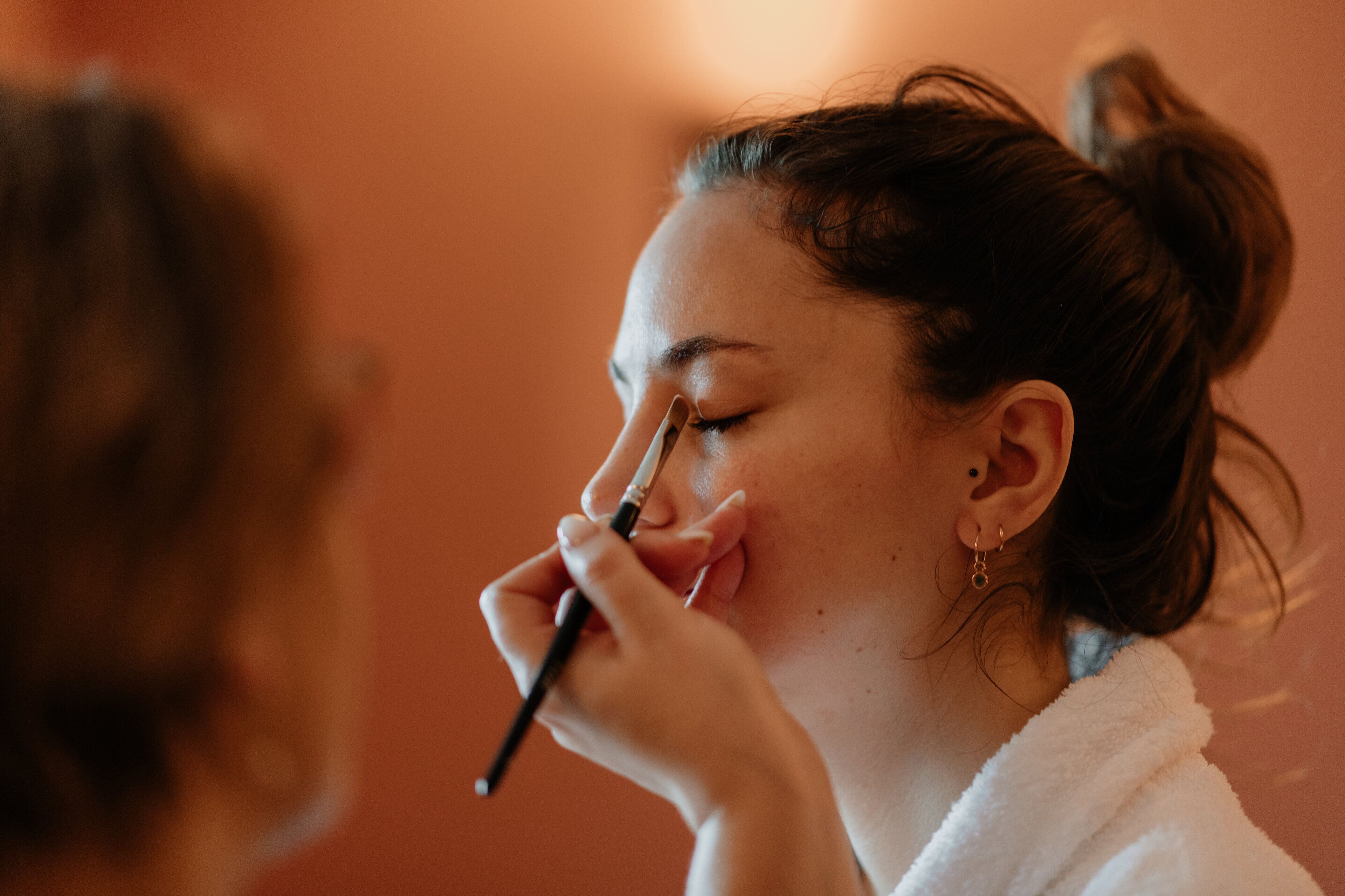 A person in a white robe holding a makeup brush.