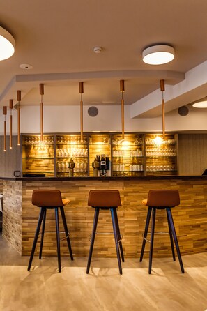 A bar area with three stools, wooden wall, and hanging pendant lights. - Waldhotel Kreuztanne (Sayda)