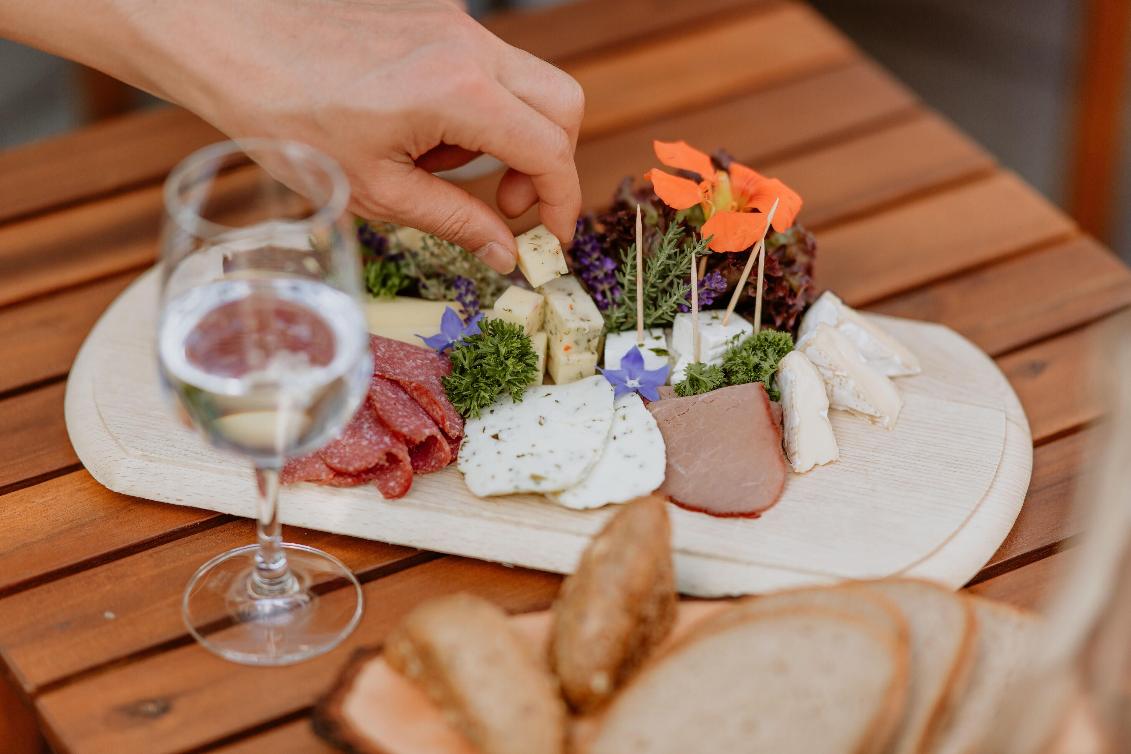 Ein Holztisch mit einer Wurst- und Käseplatte, belegt mit verschiedenen Käsesorten, Fleischwaren und Blumen.