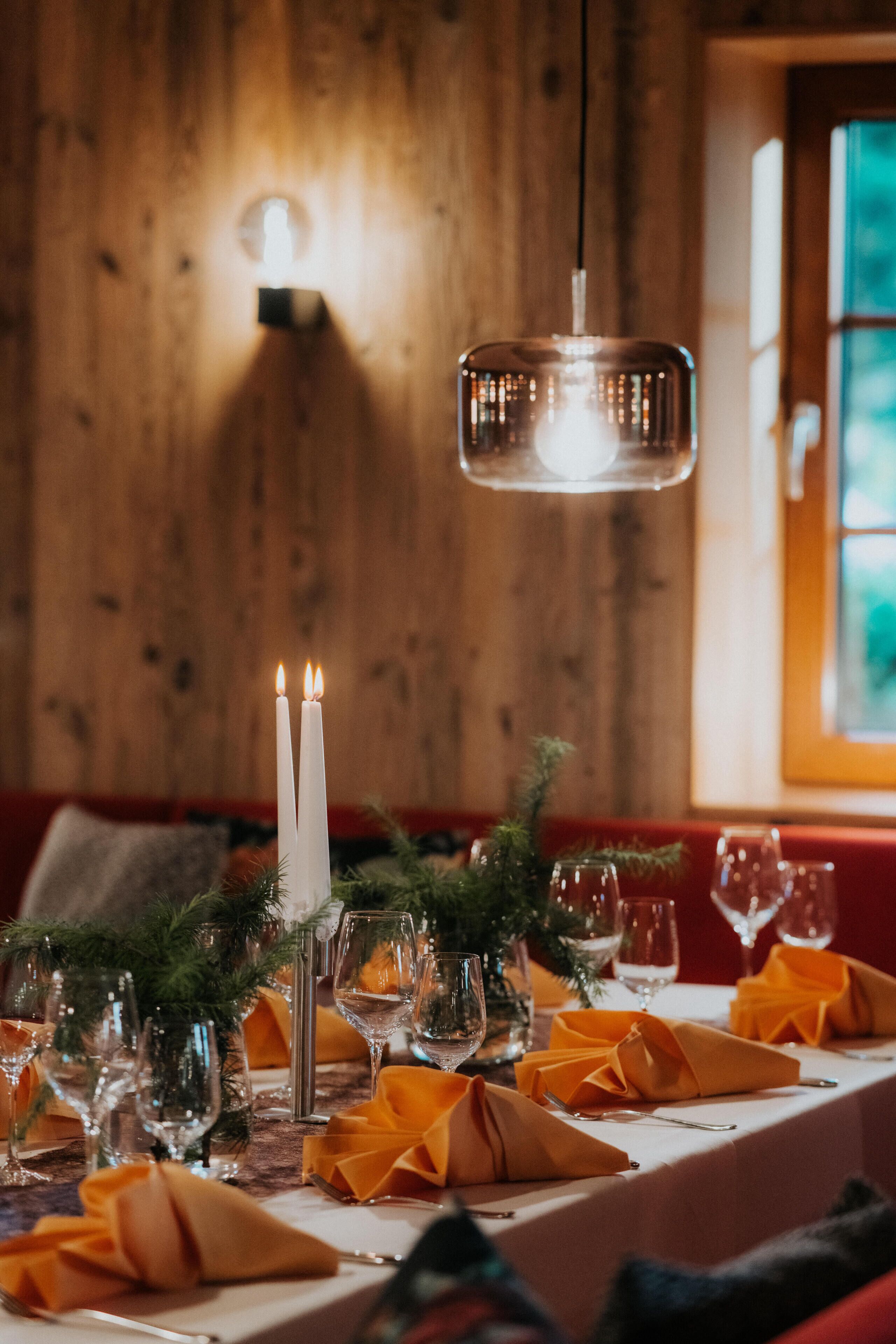 Une table dressée avec des bougies, des verres et un luminaire suspendu dans une pièce en bois.