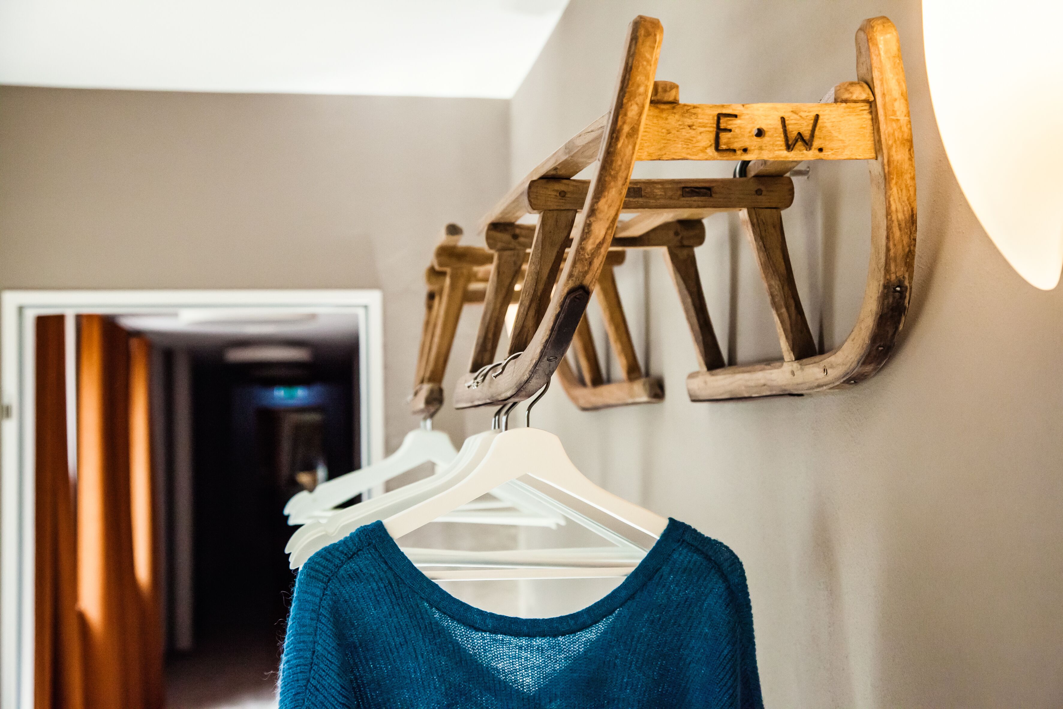 Un perchero de madera con las letras "E.W." grabadas, sosteniendo varios ganchos blancos con ropa.