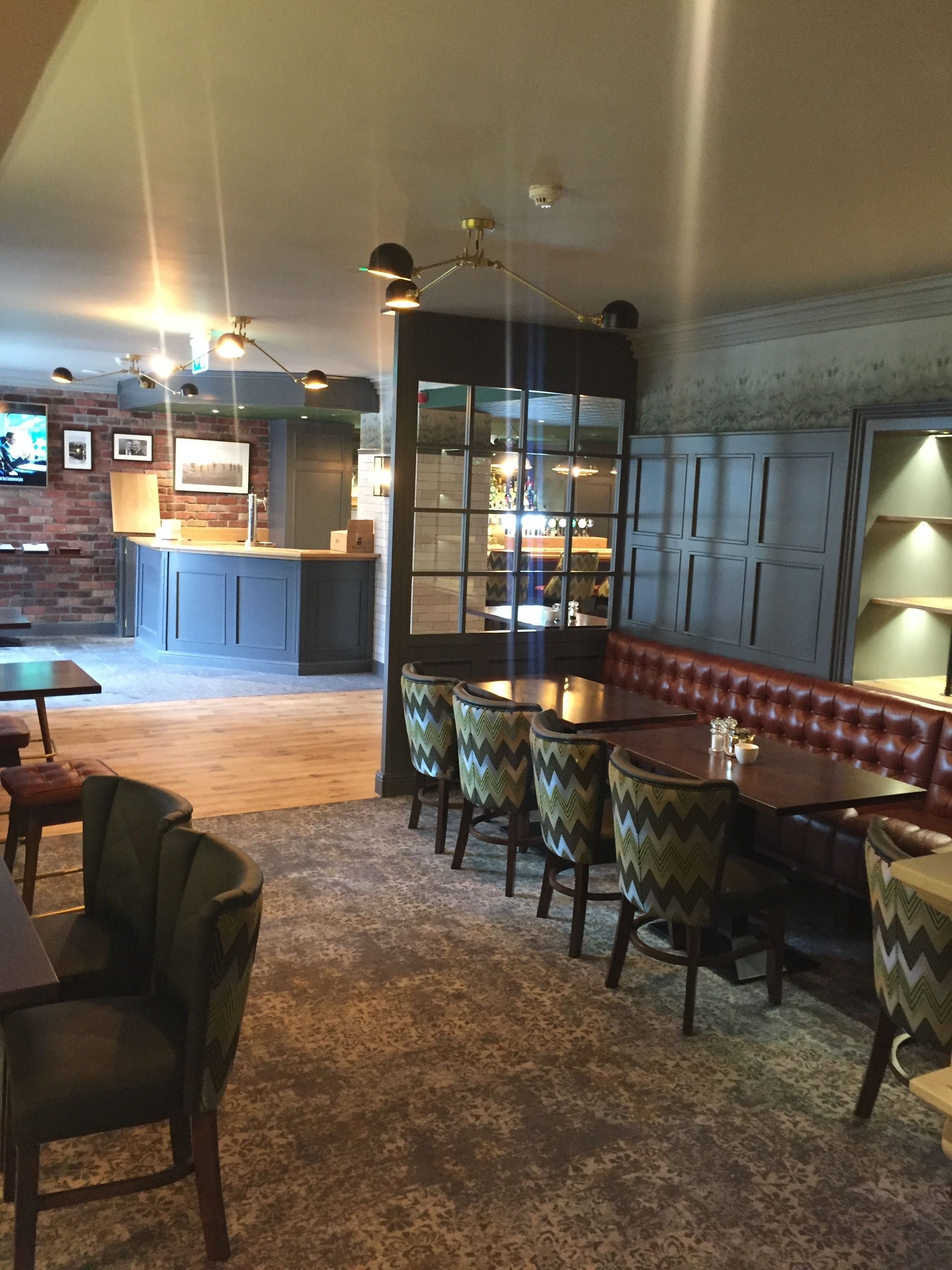 A restaurant with a bar area, seating with patterned chairs, and a wooden floor.